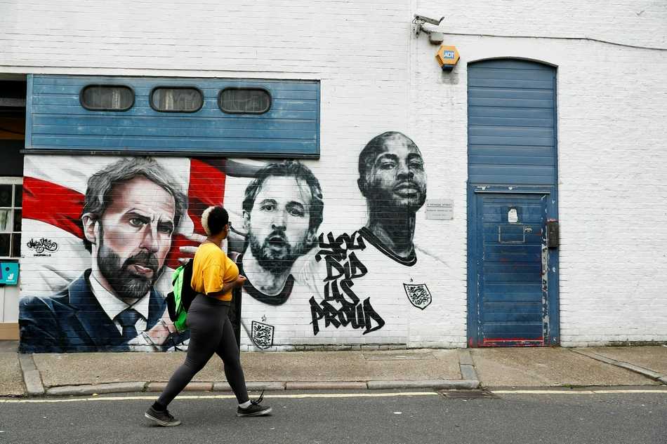 夜幕降临，街头霓虹灯下，一幅包含多名球员的群体壁画被灯光照亮，画面中的卢克·肖、斯特林等人笑容灿烂，仿佛在向过往的行人致意，为伦敦的夏夜增添了一份温暖与感动。