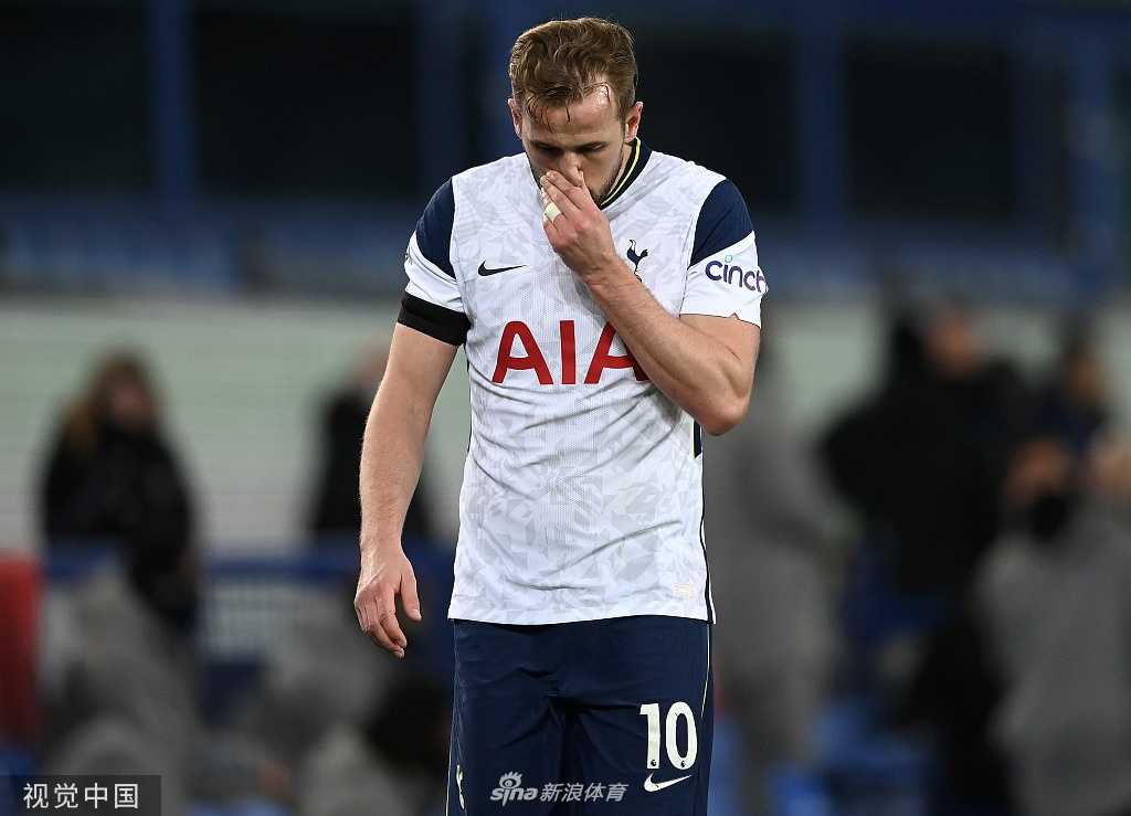 凯恩在比赛中高高跃起争顶头球，身体在空中舒展开来，像一只展翅的雄鹰，背景是虚化的对手和看台上神色紧张的球迷。