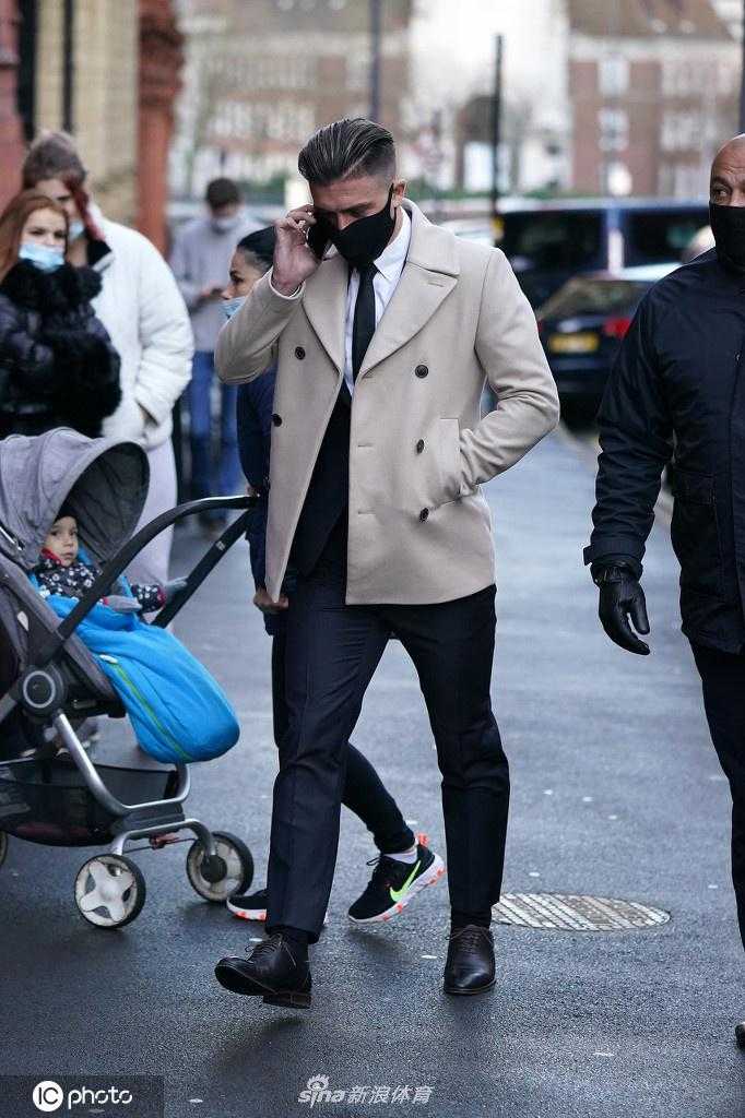 格拉利什身着深色大衣搭配奶油色双排扣外套，面戴黑色口罩，在安保人员陪同下神情严肃地步入伯明翰地方法院，面对媒体的长枪短炮显得颇为低调