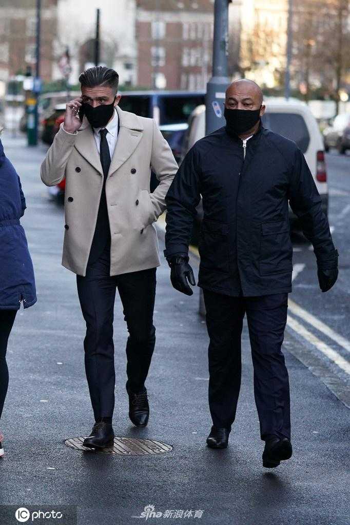 格拉利什独自一人走向法院入口，神情冷峻，身后的安保人员紧随其后。画面中他身着正装却戴着口罩，凸显了这起案件的特殊时代背景——疫情封锁与名人违法的碰撞