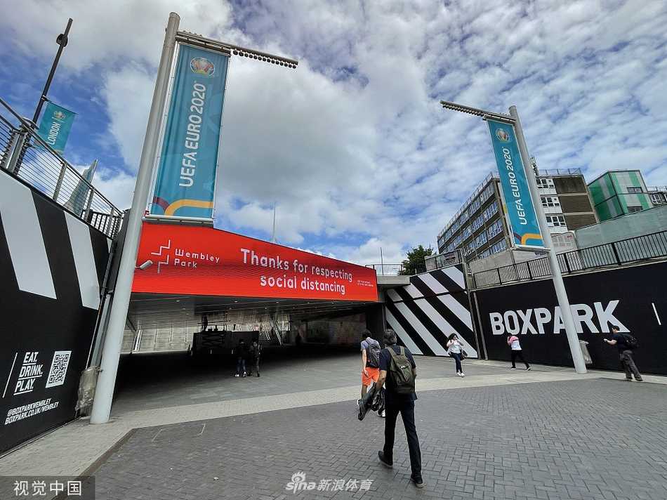 夕阳余晖如金纱般洒落在温布利球场巨大的白色拱门上，拱门的钢铁曲线在蔚蓝的天空下显得格外壮丽，仿佛一道凝固了的彩虹，静静守护着这座即将迎来无数欢呼与叹息的足球圣殿。