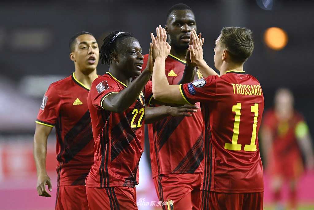 特罗萨德梅开二度后激情滑跪庆祝，他身后的看台上是挥舞着旗帜的比利时球迷，这一刻英雄与信徒同在。