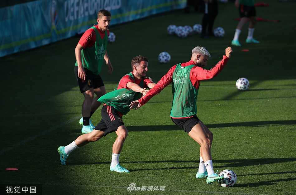 镜头拉近，一位比利时球员正在做拉伸，他紧咬球衣领口，手臂肌肉线条分明，眼神中透露出对胜利的渴望，背景是模糊的队友与异国的天空。