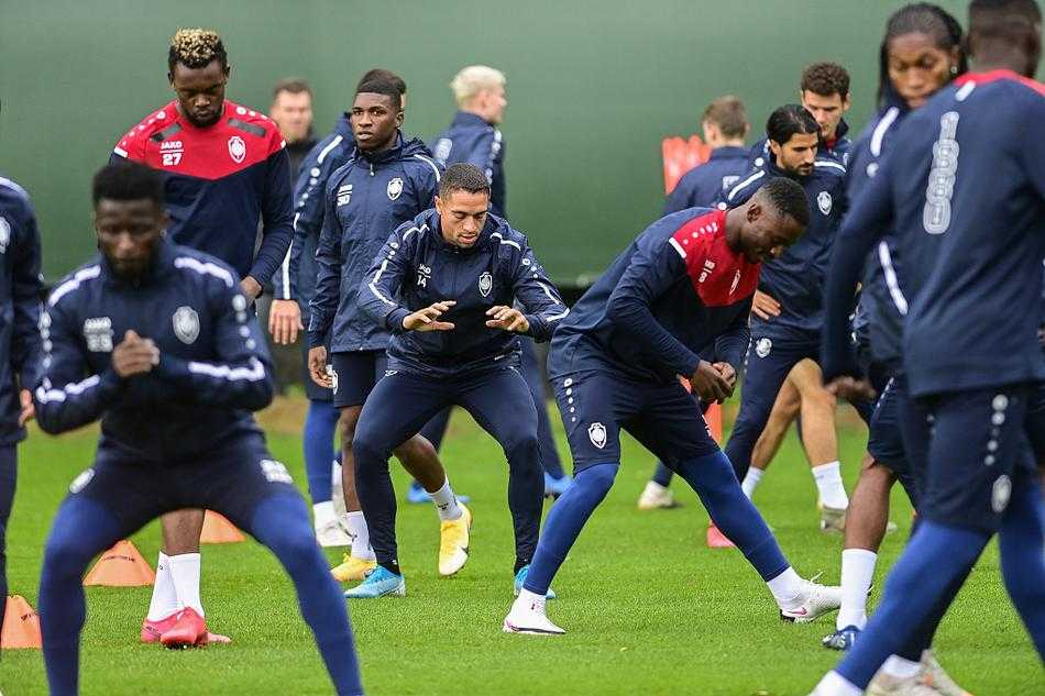 夕阳的余晖洒在训练场上，安特卫普的球员们围成一圈，手臂搭在一起，正在进行赛前最后的动员，他们的剪影充满了力量与团结的象征。