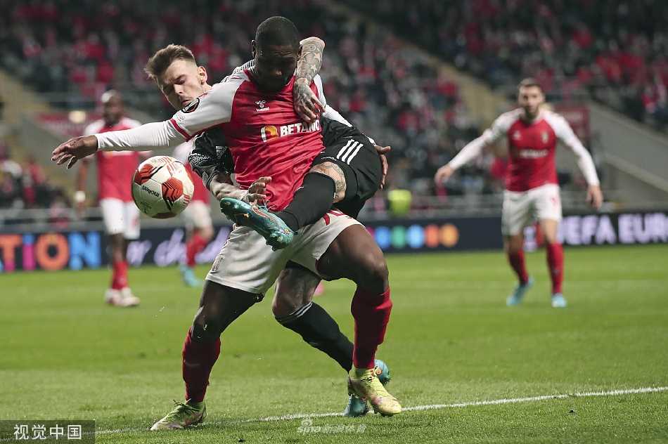 点球大战紧张瞬间，双方球员与教练在场边肩并肩站立，屏息凝神注视着球场中央决定命运的十二码点。