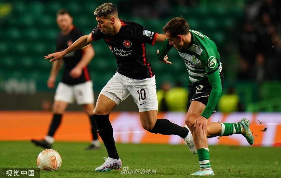 比赛激烈进行中，一名球员在拼抢后失去平衡倒地，另一名球员高举手臂向裁判示意，背景里观众席上密密麻麻的球迷正全神贯注地关注着场上局势。