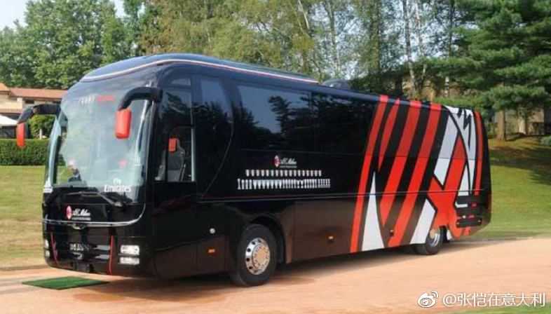 AC米兰经典红黑配色大巴，车身在阳光下闪耀着金属光泽，巨大的队徽如同盾牌，宛如一座移动的圣西罗堡垒