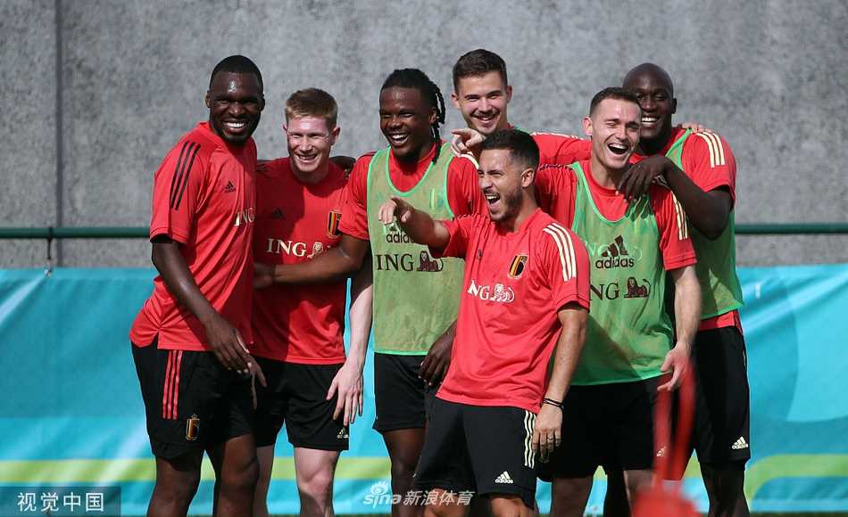 维特塞尔和默尼耶并肩而立，在训练场边驻足观看队友。默尼耶双手叉腰，神情轻松地望向远方，维特塞尔则侧身而立，嘴角挂着一丝不易察觉的微笑。背景中是模糊的球场和稀疏的观众席，整个画面充满了大战前难得的宁静与从容，将这对好友兼队友的默契定格为永恒。