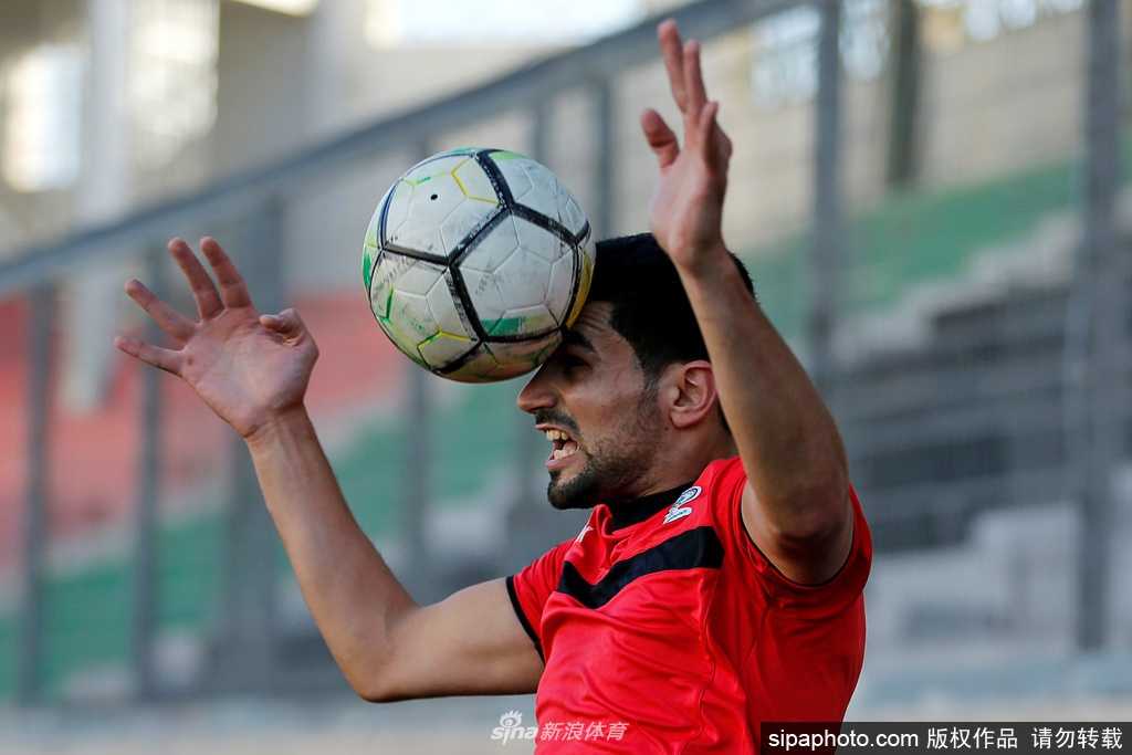 两名阿赫利球员在训练间隙，佩戴着口罩进行简短的交流，背景是迪拜特有的现代建筑群，这一幕生动地记录了疫情下足球训练的新常态。