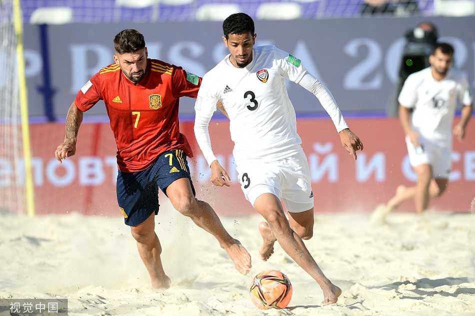 一名阿联酋球员在射门后失去重心倒在沙地上，他依然仰头紧盯着飞向球门的皮球，脸上写满了对进球的渴望。