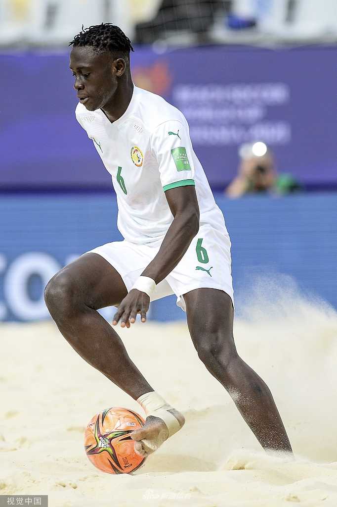 塞内加尔球员在防守中飞身封堵，身体在沙地上空舒展开来，面部肌肉紧绷，眼神坚毅，全力阻挡阿曼队的传球路线，展现了非洲冠军的顽强防守。