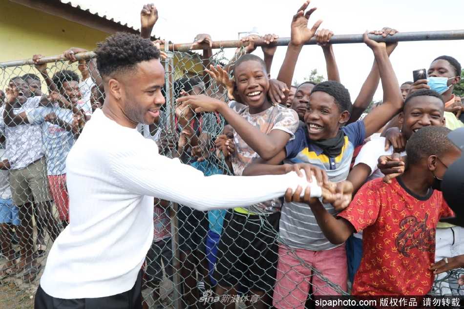 威廉王子身着黄色10号背心，在特伦奇镇的足球场上与拉希姆·斯特林欢乐传球，场边热情的当地民众将球场团团围住。