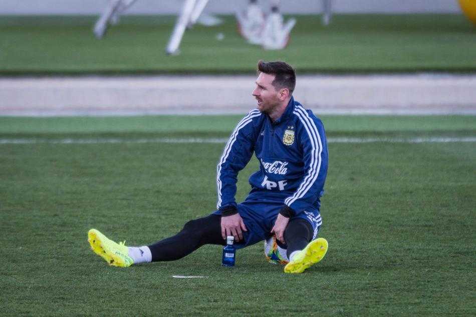 梅西与一名年轻队友在训练间隙并肩而坐，他侧身倾听队友说话，并伸出手比划着，似乎在分享一些比赛或训练中的心得与技巧。