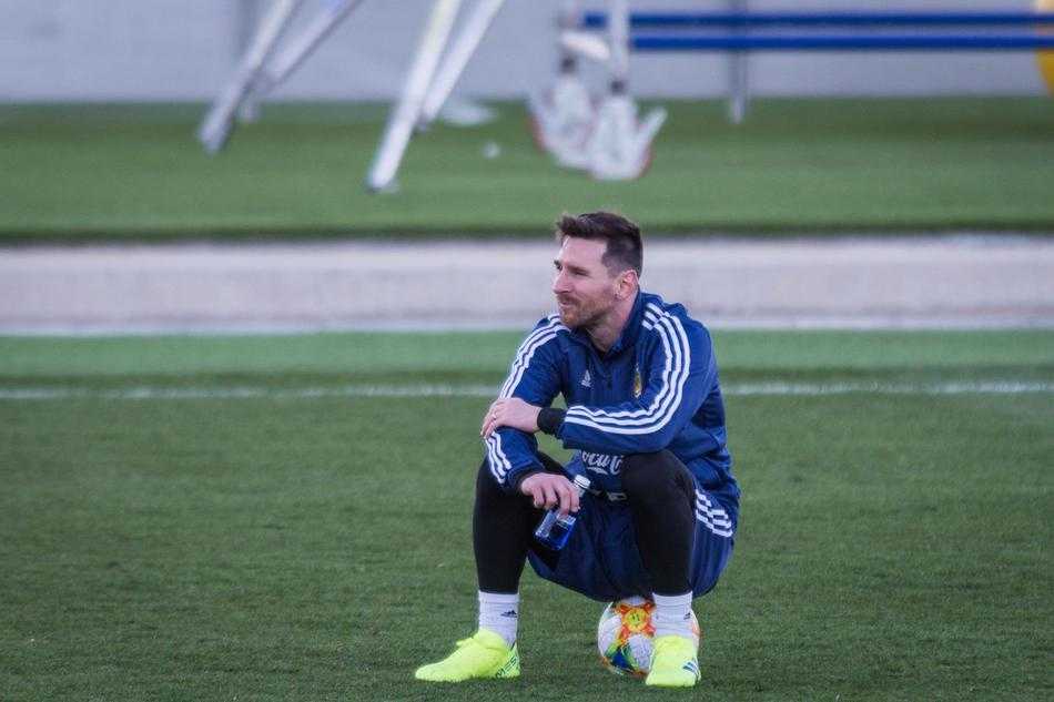 梅西身穿阿根廷训练服，悠然自得地坐在训练场的足球上，双手轻扶膝盖，眺望远方，仿佛在享受回归国家队的惬意时光。