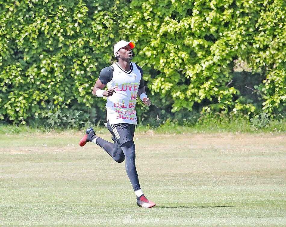 曼联球员在板球场的翠绿草坪上拉开阵型进行抢圈热身，阳光洒在他们身上，与传统足球训练场截然不同的背景板显得格外新奇。