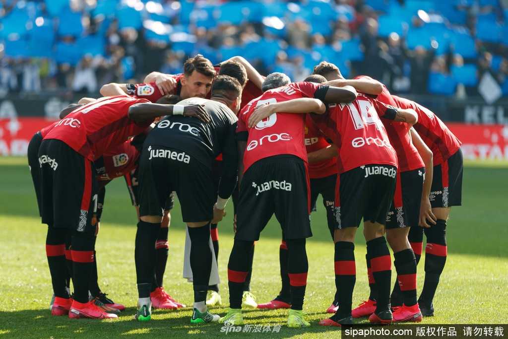 一名马洛卡球员低头缓缓走过印有俱乐部徽章的通道，身影被拉长，仿佛承载着赛季中断的无奈与对未来的思索。