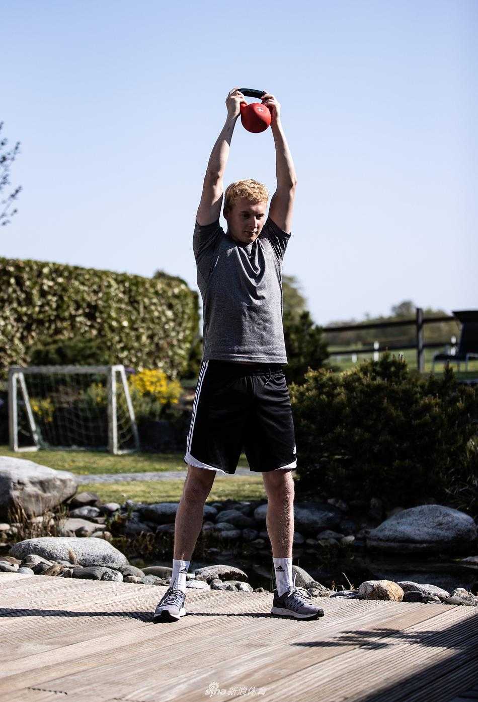 一名球员赤膊上身，在洒满阳光的阳台利用弹力带进行核心力量训练，远处的城市天际线在阳光下若隐若现。