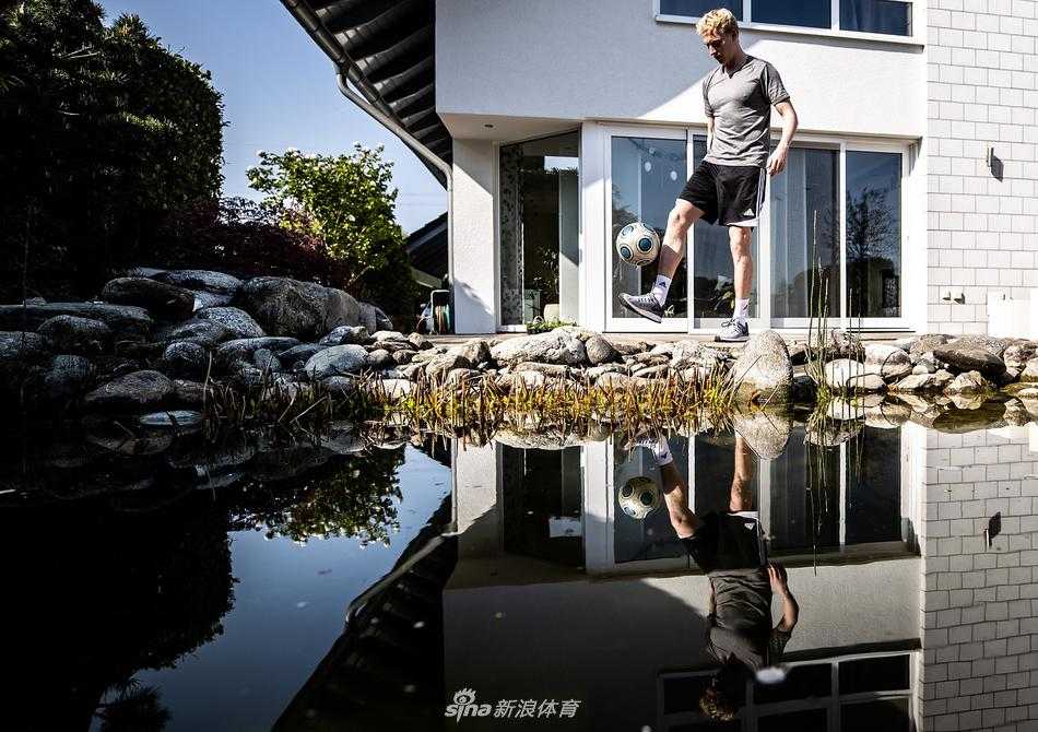 拜仁球星托马斯·穆勒在家中的跑步机上慢跑，他面带微笑对着镜头竖起大拇指，客厅的一角摆放着孩子的玩具，温馨又充满活力。