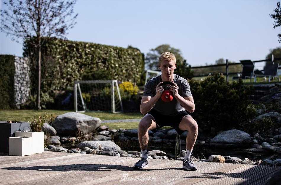 博阿滕赤裸上身，戴着耳机在家中健身房伴随着动感音乐进行负重深蹲，墙壁上的镜子映出他专注而坚毅的表情。