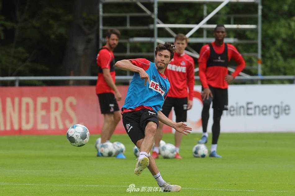 科隆球员在训练中高高跃起，准备用胸部停球，他的动作舒展而有力，远处的教练组成员同样戴着口罩密切关注，这不仅是技术的练习，更是对重回赛场的迫切心情的释放。