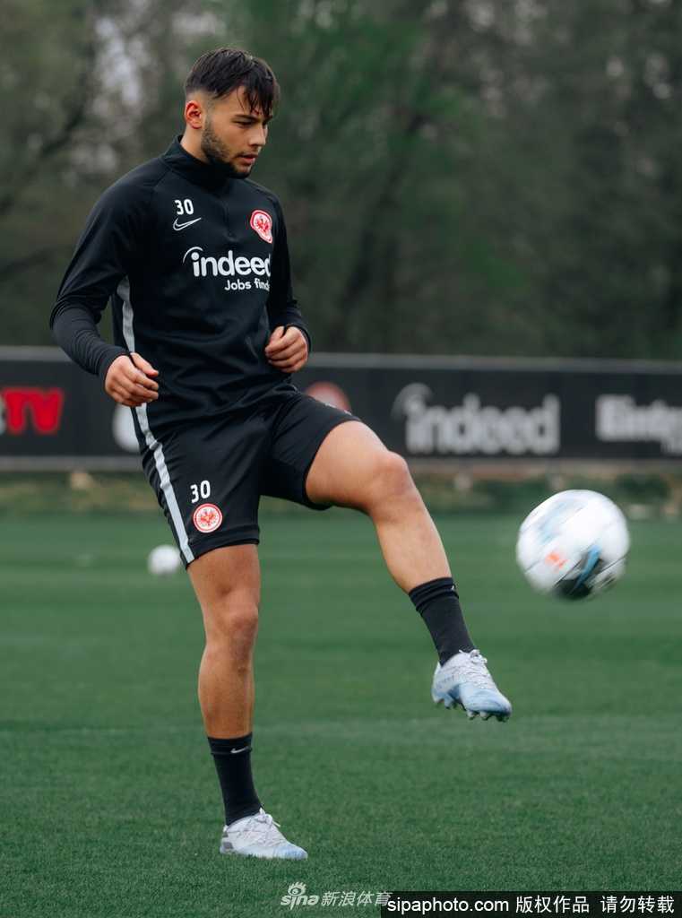 阳光洒在绿茵场上，一名法兰克福球员正在进行高强度的绕杆训练。他的眼神坚毅，肌肉线条在运动服下绷紧，预示着随时准备为即将到来的战斗倾尽全力。