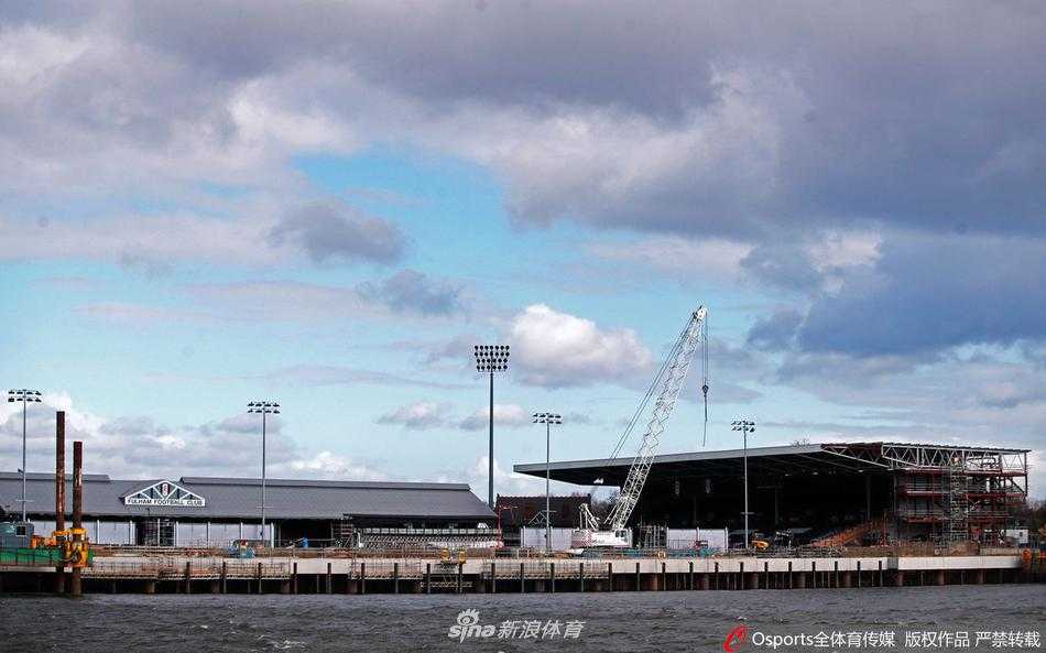 一名戴着口罩的工人独自站在工地的建材堆旁，目光望向远方，他的身影在庞大的工程框架下显得渺小，无声诉说着疫情之下个体与时代的共同困境。