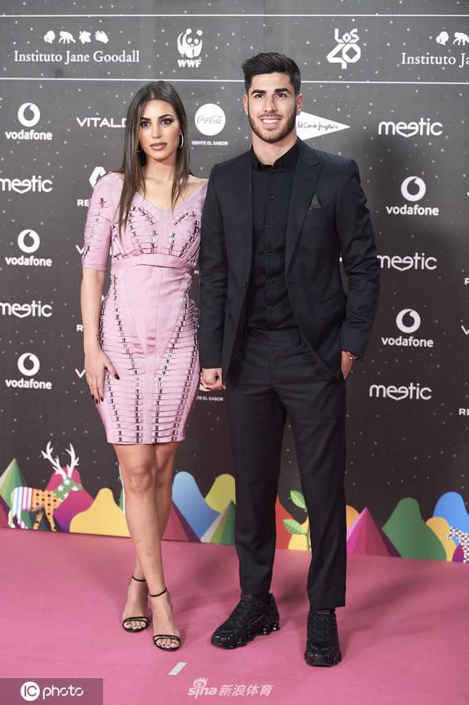 镜头拉近，阿森西奥的下颌线在灯光下显得格外硬朗，他侧耳倾听女友低语。桑德拉的眼妆闪烁着细碎的亮光，红唇微启，这一刻的亲密无间仿佛隔绝了红毯外的嘈杂。