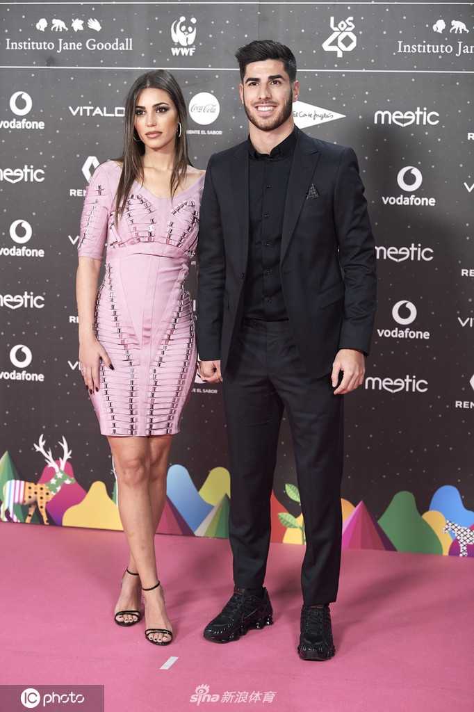 桑德拉一袭修身长裙勾勒出完美身形，她微微侧身面向镜头，妆容精致，笑容自信而从容。阿森西奥则在她身后半步，温柔地注视着她，仿佛在看自己最得意的奖杯。