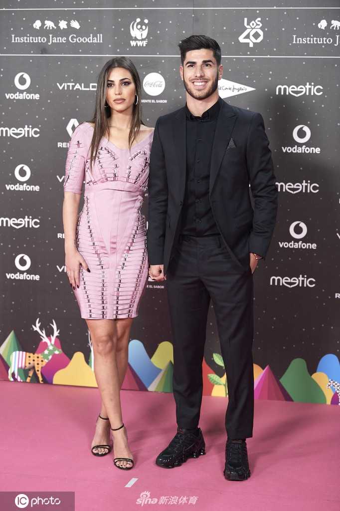 两人在颁奖礼内场并肩而坐，阿森西奥身体微微倾向女友，似乎在讨论刚刚过去的某个有趣环节。桑德拉手拿精致的晚宴包，专注地聆听，两人之间形成了旁人无法介入的气场。