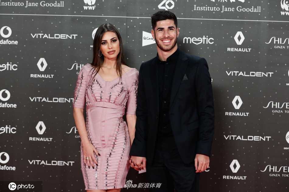 两人在巨大的品牌背景板前留下正式合影，阿森西奥一手轻揽女友的腰肢，桑德拉则手持邀请函，姿态优雅。俊男美女的组合，与身后璀璨的颁奖礼灯光融为一体，构成一幅完美的画面。