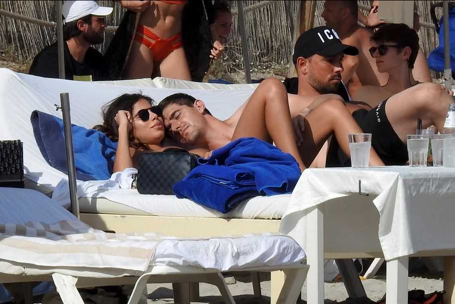 库尔图瓦赤裸上身躺在沙滩椅上，女友米歇尔亲密地趴在他的胸口，以他宽阔坚实的胸膛为枕，两人相视而笑，阳光洒在身上，画面满是柔情蜜意。