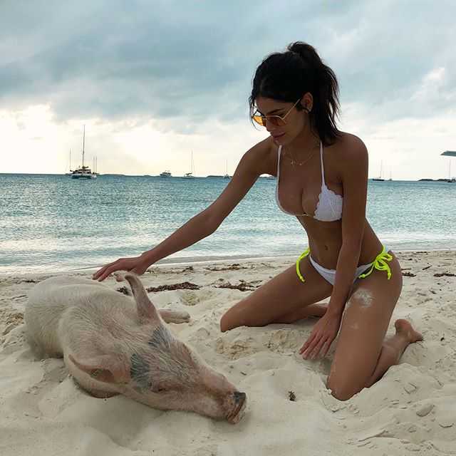 库尔图瓦戴着墨镜，穿着休闲印花衬衫，单手搂着女友的腰。米歇尔穿着白色比基尼搭配轻盈的沙滩裙，两人站在海边的礁石上，身后是蔚蓝无垠的大海，笑容灿烂如阳光。