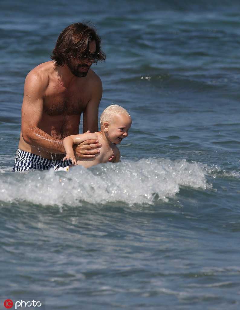 抱着儿子站在浅滩中，皮尔洛的背影充满了力量感，这背影曾扛起过意大利足球的荣耀，如今只愿为孩子遮风挡雨，撑起一片无忧无虑的天空。