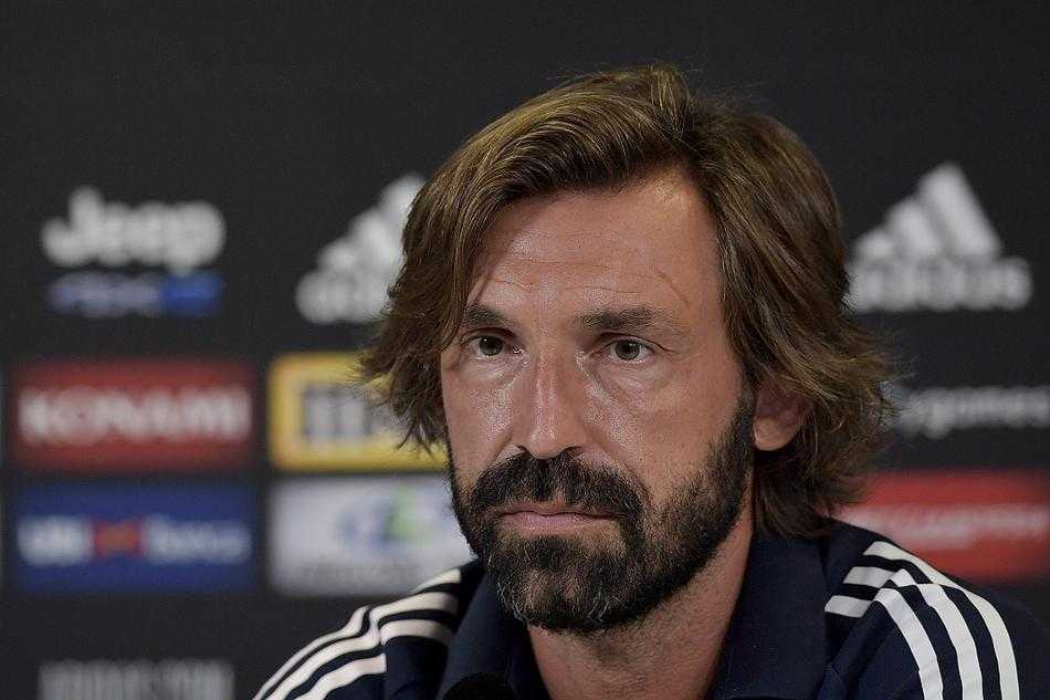 发布会现场的皮尔洛正在进行手势讲解，他身体微微前倾，右手抬起食指指向空中，仿佛正在向球员们布置战术，背景板上的尤文图斯队徽与他意气风发的神态相得益彰。