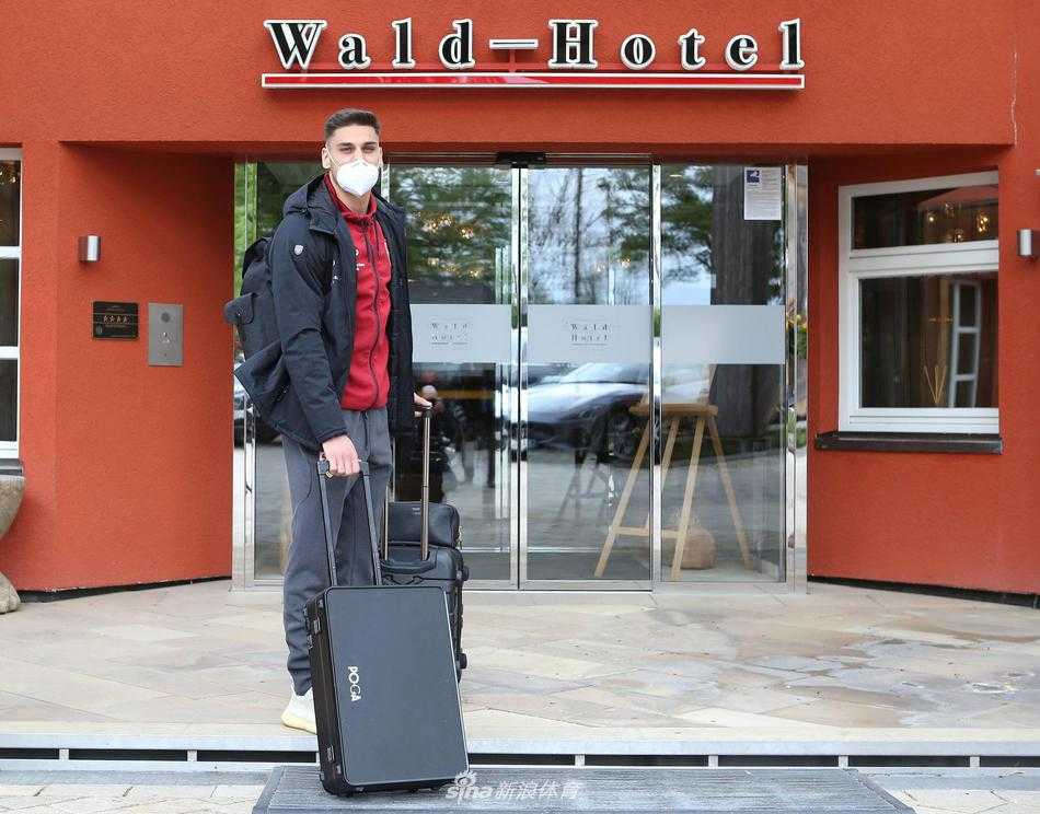 一名年轻球员提着行李独自步入旋转门，瘦削的背影在偌大的玻璃门前显得格外坚定，象征着球队未来的希望