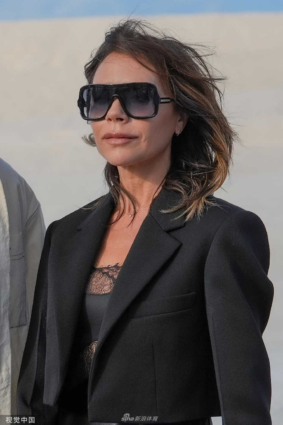 维多利亚与身旁嘉宾微笑交流，一袭黑衣在众多浅色着装中脱颖而出，彰显其无可争议的现场焦点地位。