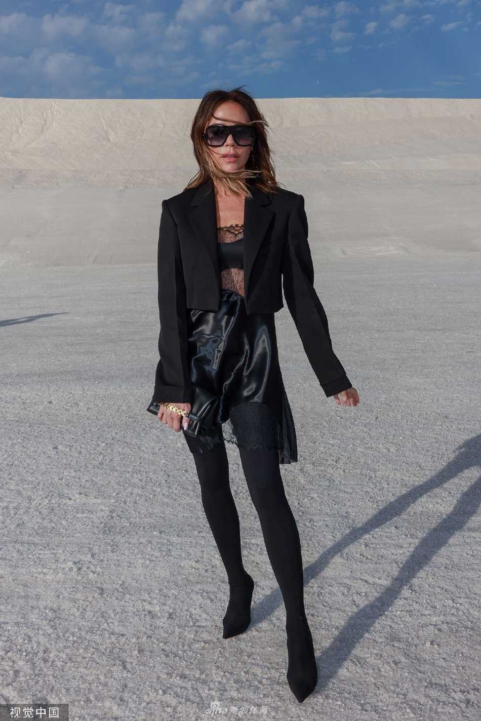 维多利亚漫步于盐田秀场，步履坚定，黑色身影在广阔天地间显得既孤独又强大，仿佛时尚世界的探险家。
