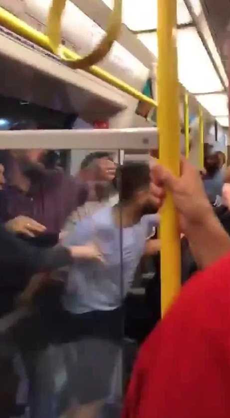 打斗从站台延续到了车厢内部，狭小的空间内人们推搡拉扯，有人摔倒在地铁地板上，旁边是冷眼旁观的无奈乘客。