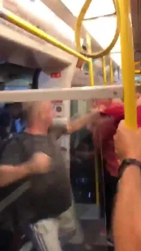 一名身着便装的球迷被推倒在站台边缘，手中疑似还握着酒瓶，周围的人视若无睹，只有列车车门静静地见证着这场闹剧。