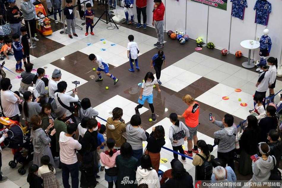 一名小男孩在成功完成一次射门后，兴奋地高举双臂，脸上绽放出无比灿烂自豪的笑容。在他身后，是密密麻麻的围观人群，不少人举着手机记录下这充满成就感的瞬间，整个商场仿佛都为这个孩子的快乐而喝彩。