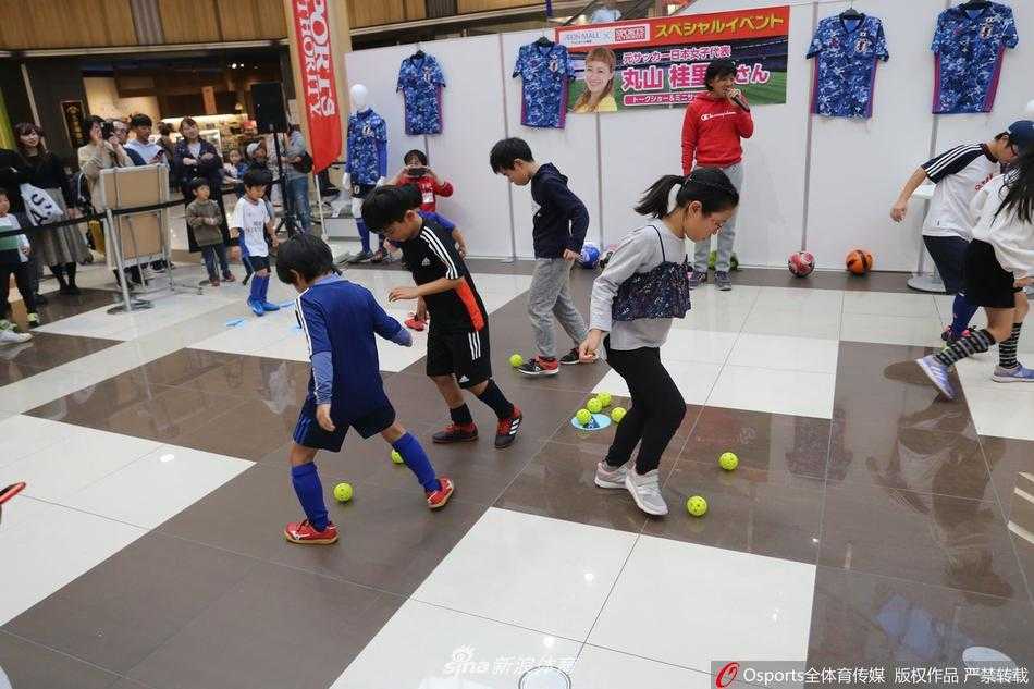 一位年纪稍长的指导者正蹲在地上，耐心地为一名小球员讲解动作要领。孩子仰着头，听得聚精会神。周围其他的小队员们或坐或站，也在认真地观摩学习，画面充满了传承与教导的温情。