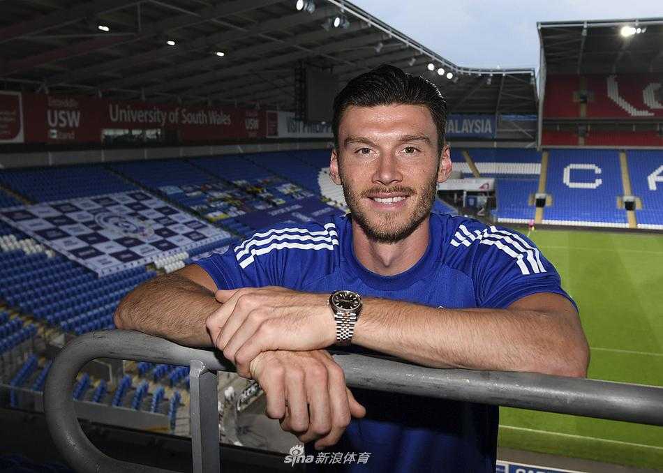 基弗·穆尔在卡迪夫城训练基地的办公室里，微微侧身与俱乐部工作人员亲切交谈，他身着便装，神情专注而放松，墙上悬挂着球队的历史照片，营造出浓厚的职业氛围。