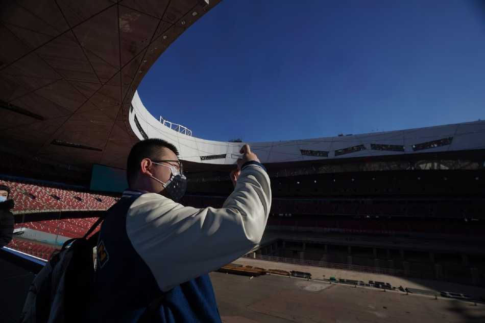 国家游泳中心“冰立方”的冰场上，阳光透过玻璃幕墙洒下斑驳的光影，几位身穿红色马甲的冬奥志愿者正弯腰推着冰壶，眼神专注，体验着冰壶运动的魅力，场馆内的欢声笑语与冰壶滑行的清脆声响交织在一起。