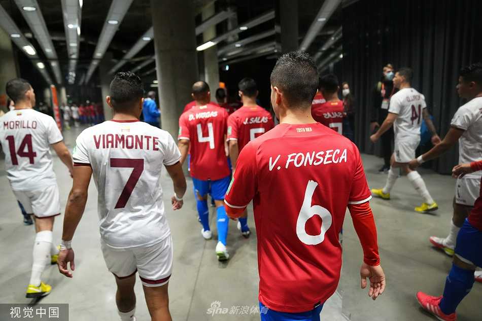 场边，委内瑞拉的教练组成员们身体前倾，目光如炬，他们的手臂在空中比划着战术，脸上写满了紧张与期待。身后看台上模糊的观众与鲜艳的旗帜，烘托出世界杯赛场的独特氛围。