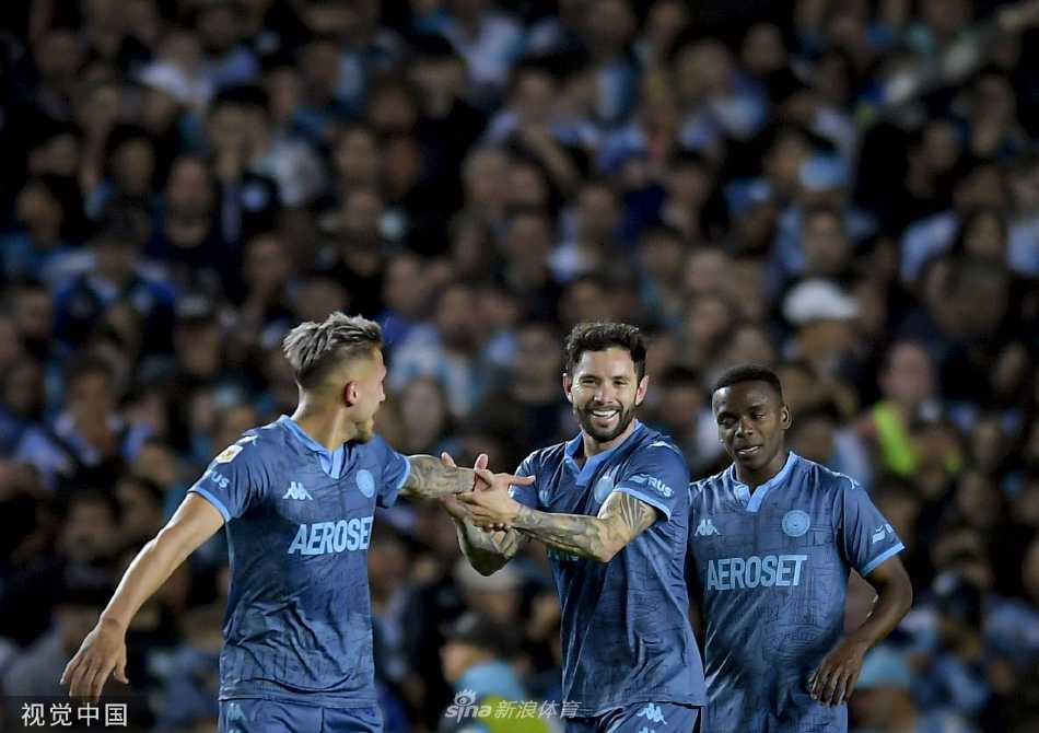 竞技队球员恩佐·科佩蒂在进球后张开双臂，面向看台激情庆祝，队友从身后飞奔而来准备拥抱他