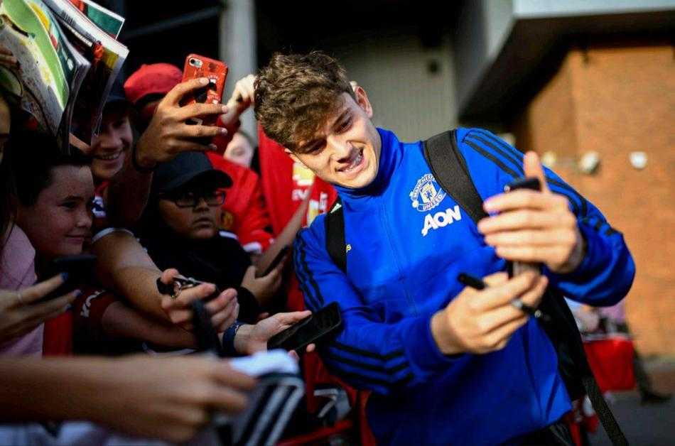 从高处俯瞰老特拉福德外的球迷区，人头攒动但秩序井然，曼联的红色围巾在看台上连成一片海洋，索尔斯克亚的身影在人群中央，正在与四面八方的球迷互动