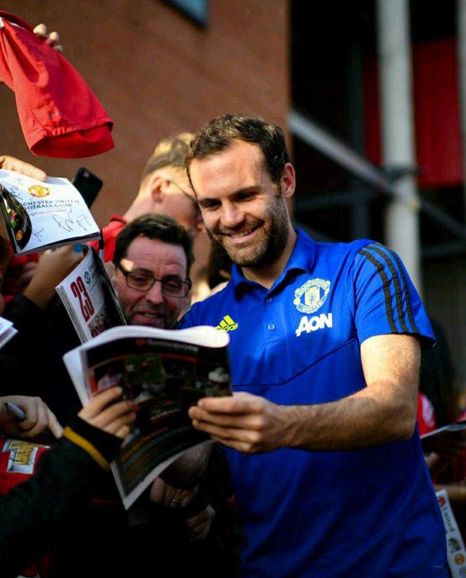 一位曼联小球迷骑在父亲的肩膀上，努力伸出手想要触碰索尔斯克亚的手，索帅踮起脚尖微笑着回应这个充满童真的请求，周围的球迷纷纷用手机记录下这一暖心时刻