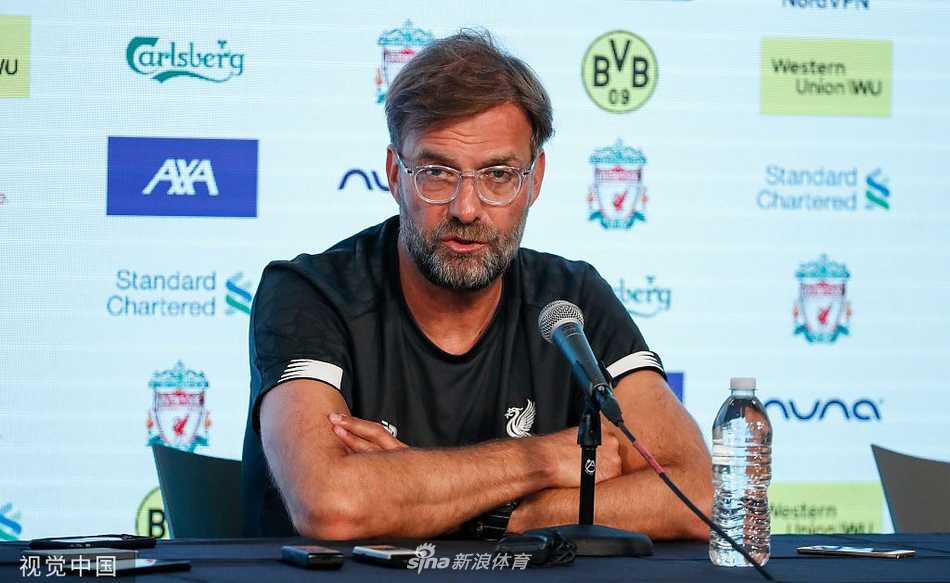 克洛普在美国夏日的阳光下，双手插兜，面带标志性笑容，目光深邃地注视着远方的训练场。