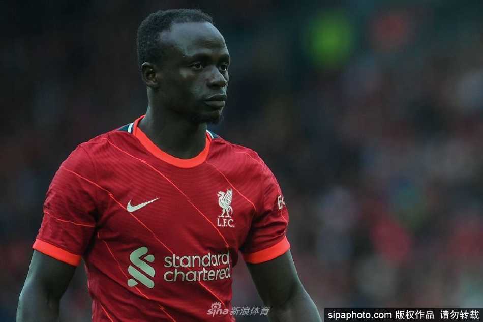塞内加尔球星萨迪奥-马内身披利物浦战袍，在安菲尔德球场的聚光灯下露出标志性的淳朴微笑，眼神中透露出对未来的坚定与忠诚。