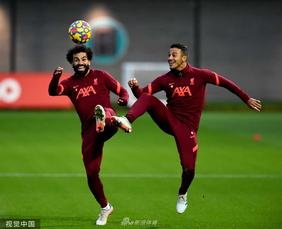 克洛普穿着标志性的棒球帽和训练服，双手叉腰站在场边，神情专注地观察着训练赛，身后是开阔的训练基地和绿树。